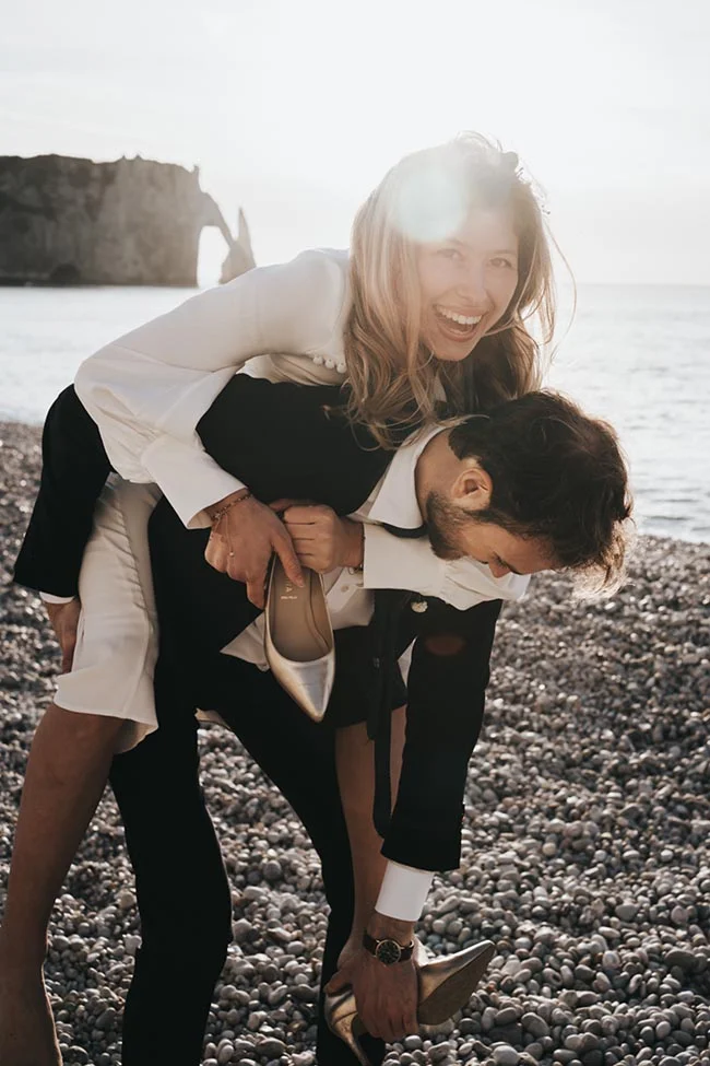 Un couple heureux se détache sur une plage rocheuse, vêtu de costumes de mariée et d'homme, pour un mariage en petit