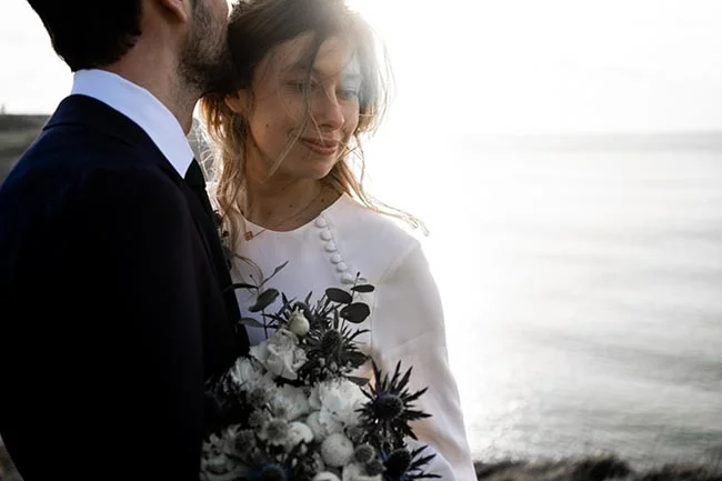 Un couple heureux près de la mer, le mari en costume noir et le mariée en robe blanche avec un bouquet noir et blanc,