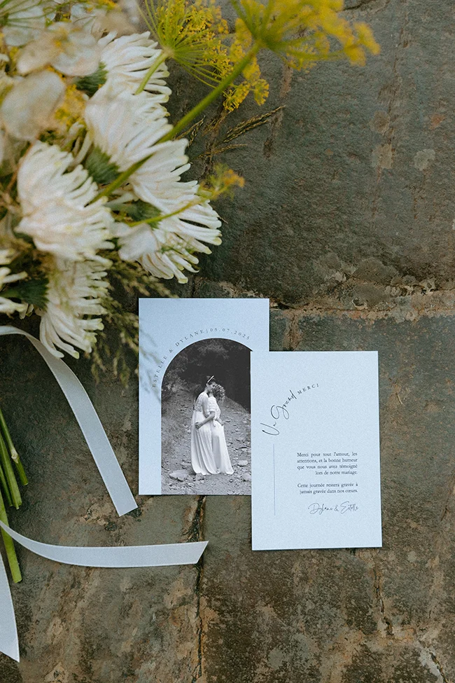 Un couple romantique dans les Pyrénées, avec invitations et fleurs soigneusement disposées sur un fond rustique.
