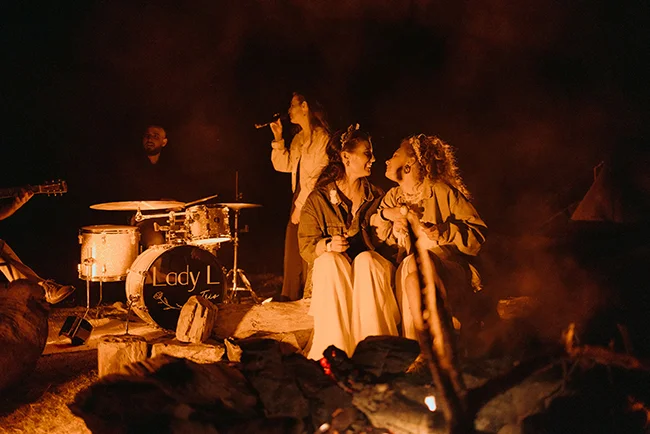 Une scène chaude et intime d'un couple qui se détend au pied d'un feu de camp, entouré d'un groupe de musiciens qui les