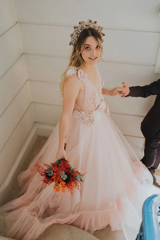 Une jeune mariée dans un magnifique robe de mariage rose, ornée de fleurs blanches et de bordures en tulle, tenant un