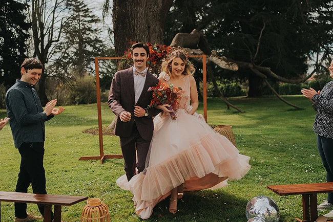 Une jeune mariée dans un robe de mariage rose floue et un mari à la cravate rose, marchant main dans la main dans un