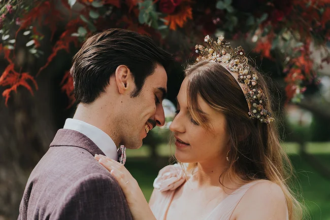 Un couple charmant se penche l'un envers l'autre, souriant tendrement sous les feuilles rouges, dans un instant