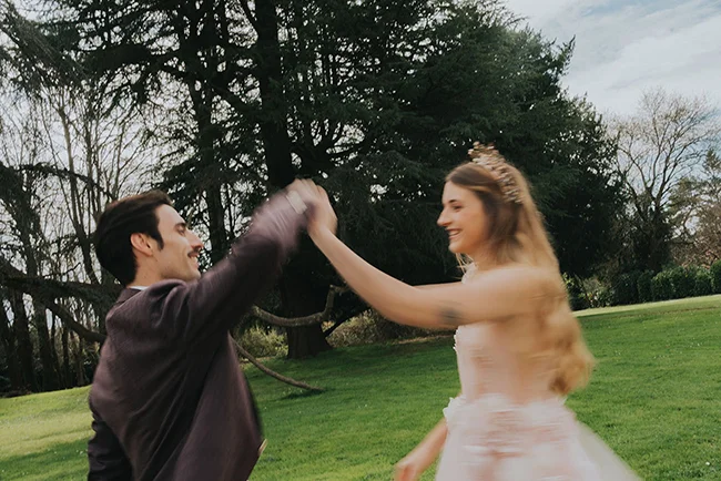 Une jeune mariée dans un robe blanche légère et un mari en costume sombre dans un parc luxuriant, célébrant leur