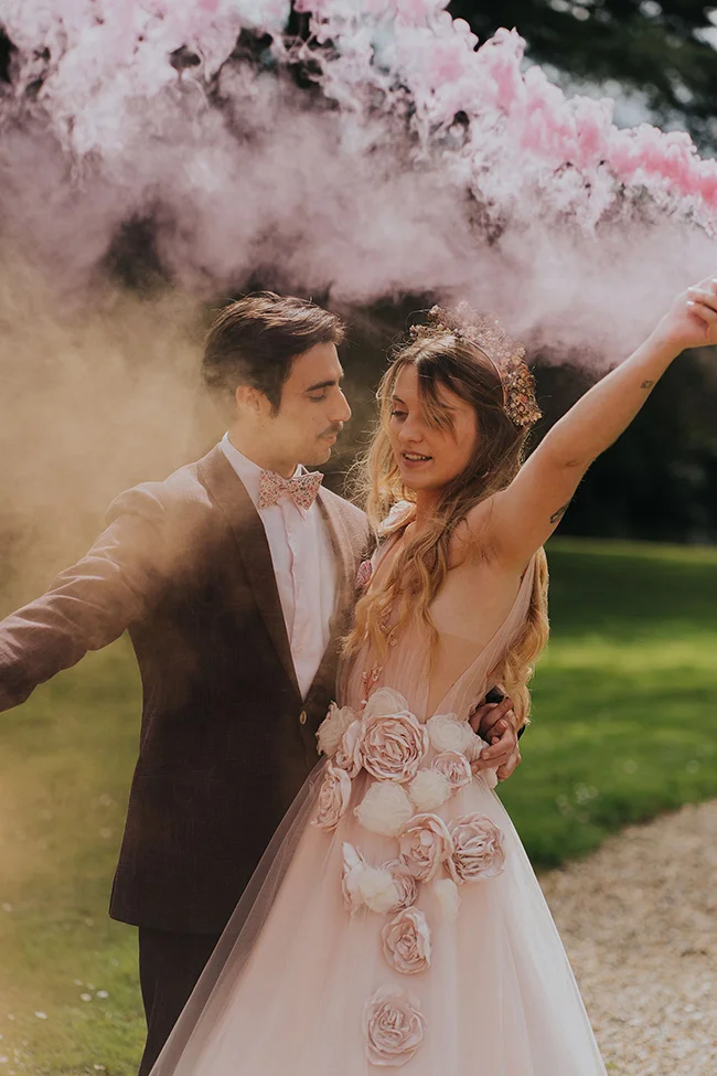Un couple heureux dans des costumes élégants et romantiques, entouré de nuages de fumée rose, symbolisant l'atmosphère