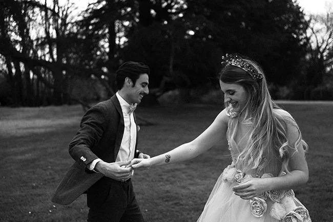 Un couple heureux dans des costumes de mariage classiques, partageant un moment tendre dans un parc luxuriant.
