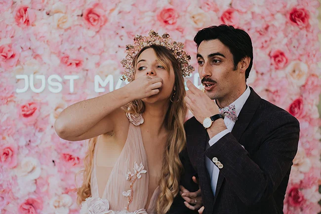 Un couple heureux en face d'un fond de fleurs roses, célébrant leur mariage populaire et romantique.