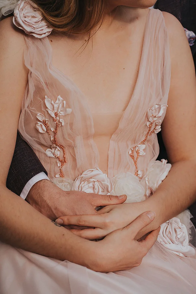 Un couple tendrement s'embrassant, la mariée dans une robe époustouflante de voile rose ornée de fleurs et de perles.