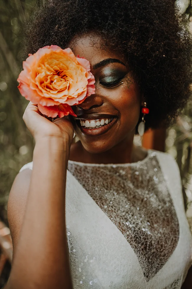 Une mariée éclatante et heureuse tient un fleur de roses orange, son sourire captivant contre un fond naturel.