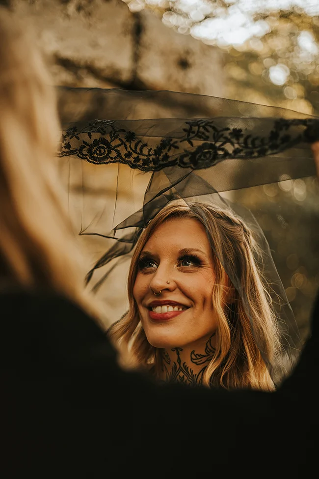 Une mariée éclatante avec une teinture sombre et une cape de mariage ornée de dentelles noires.