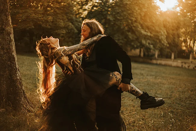 Un couple élopé partage un moment romantique dans un parc ensoleillé, leurs tattoos et vêtements sombres ajoutant un