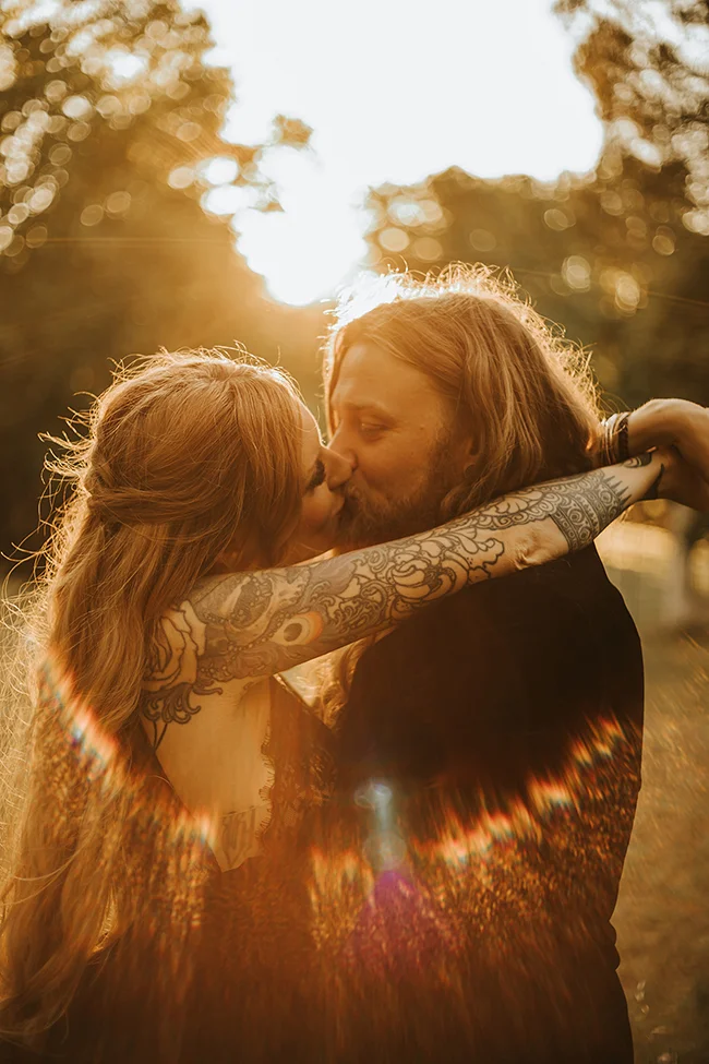 Un couple romantique partage un baiser tendre au coucher de soleil, leurs tatouages ornant leur corps, incarnant