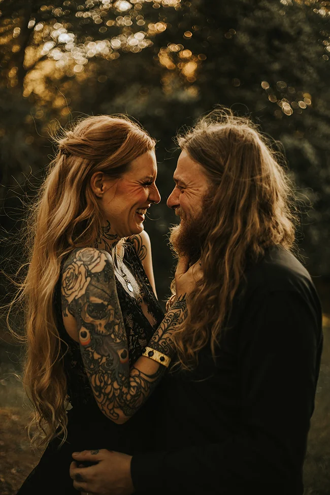 Un couple élopé partage un moment intime dans un décor sombre et romantique, leurs tatouages et vêtements sombres
