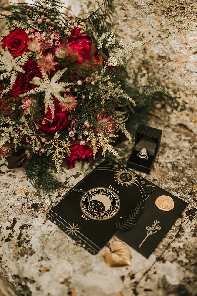 Un bouquet romantique de roses rouges et fleurs blanches entoure un livre de divination sombre, symbolisant un mariage