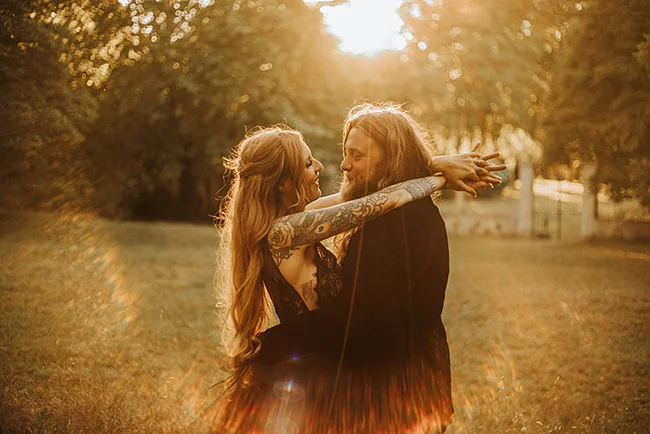 Un couple romantique partage un moment tendre dans un parc ensoleillé, leurs tatouages se révélant dans la lumière.