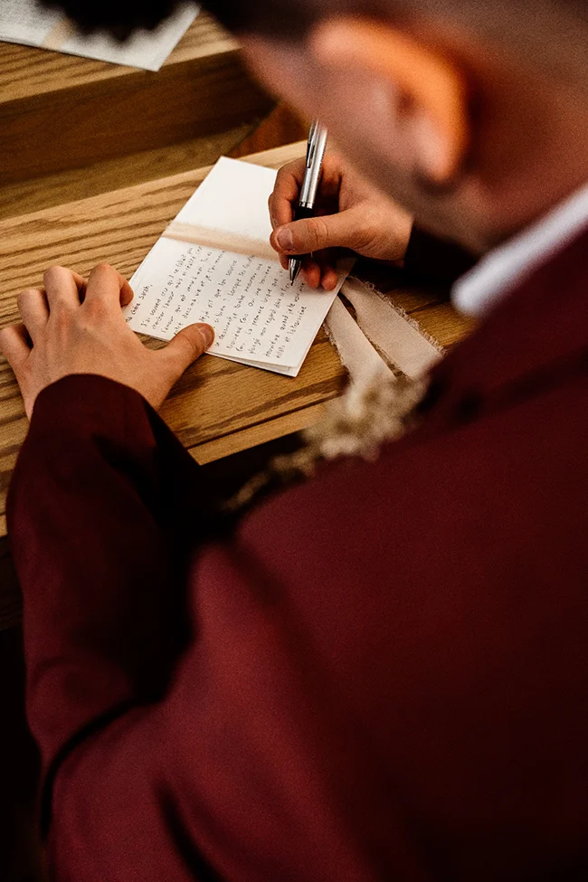 Un mari en costume rouge écrive un message intime sur un petit cahier, ambiante intime et romantique.