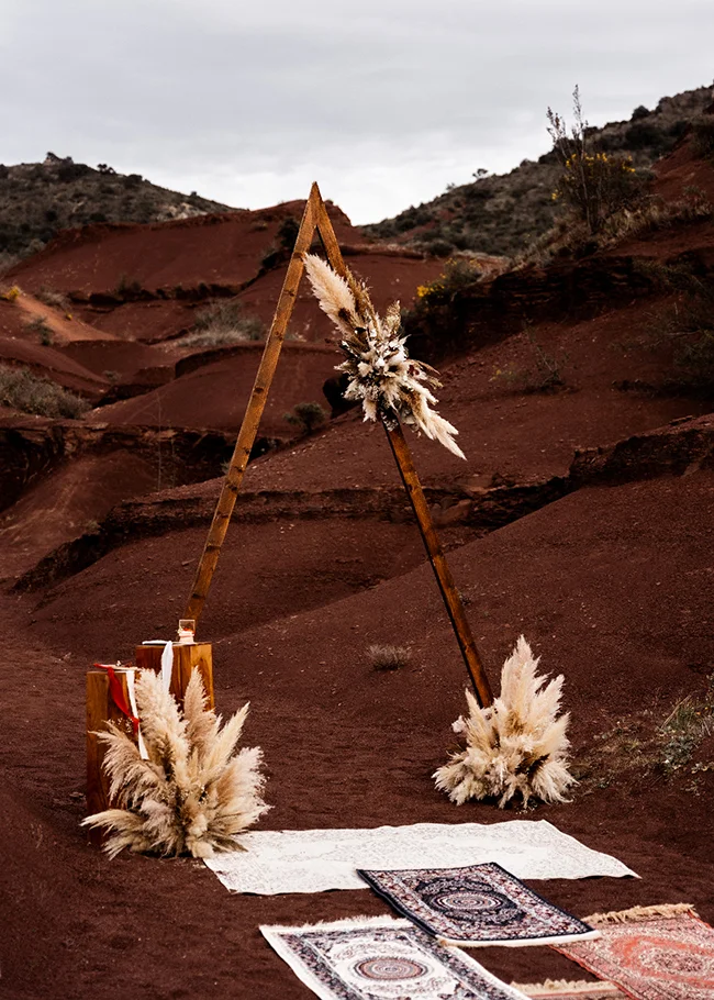 Scène romantique d'un mariage bohème au canyon du Diable, avec un arc décoratif en bois et des tapis colorés.