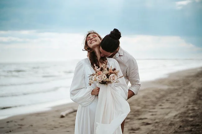 Une jeune mariée blanche déguste l'émotion avec son compagnon sur la plage de la Camargue.
