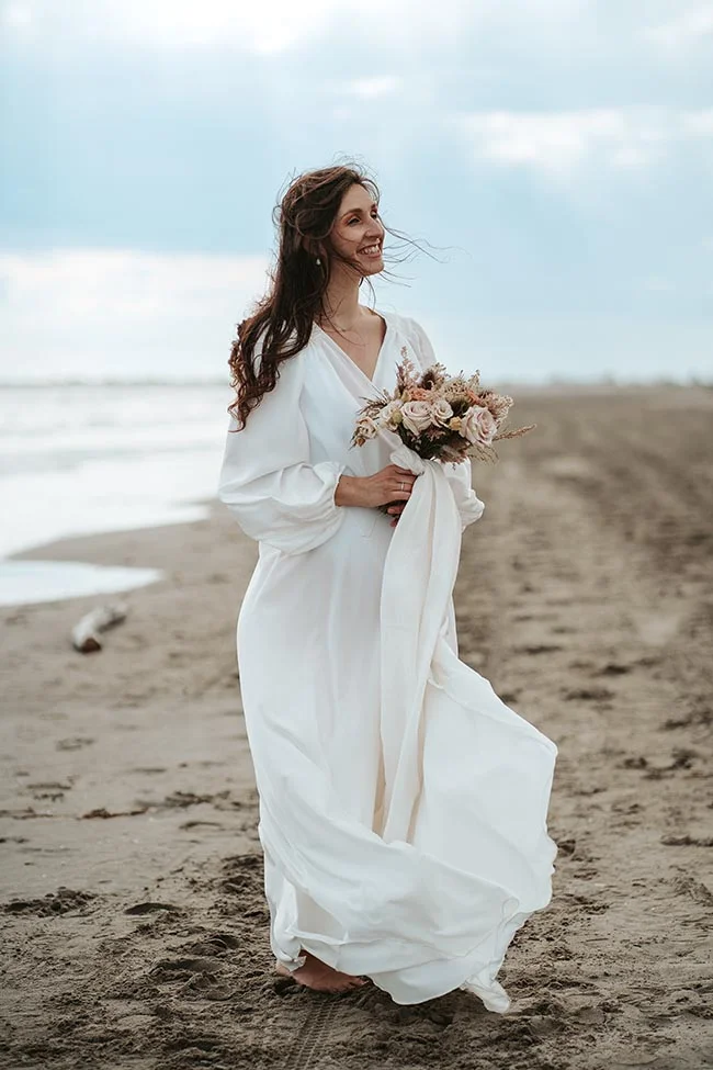 Une mariée blanche éclatante se promène sur la plage de la Camargue, tenant un bouquet de fleurs douces, capturant