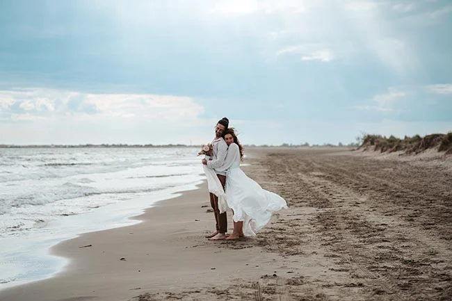 Un couple éloping romantique sur la plage de la Camargue, célébrant leur amour avec des vêtements blancs flous et une