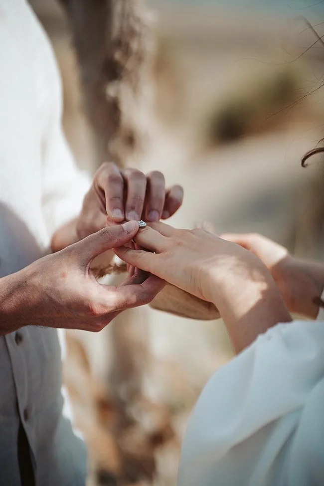 Un couple en amour partageant un moment intime au bord de la mer, échangant des anneaux de mariage.