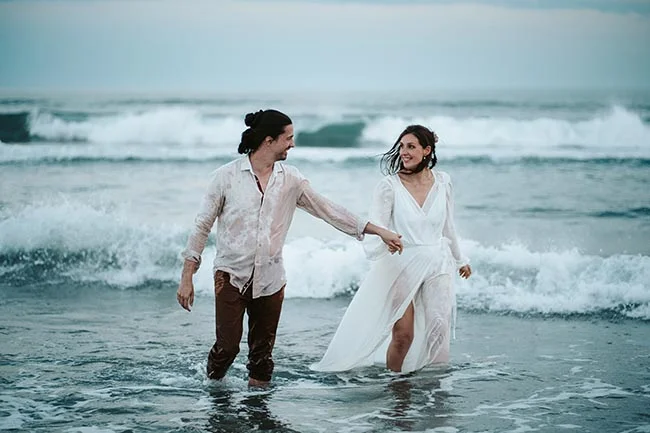 Un couple éblouissant se promène dans l'océan, leurs vêtements blancs dansant avec les vagues, symbolisant l'innocence