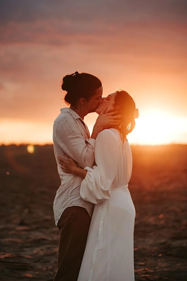 Un couple romantique partage un baiser tendre contre un ciel d'or au coucher de soleil sur la plage de la Camargue.