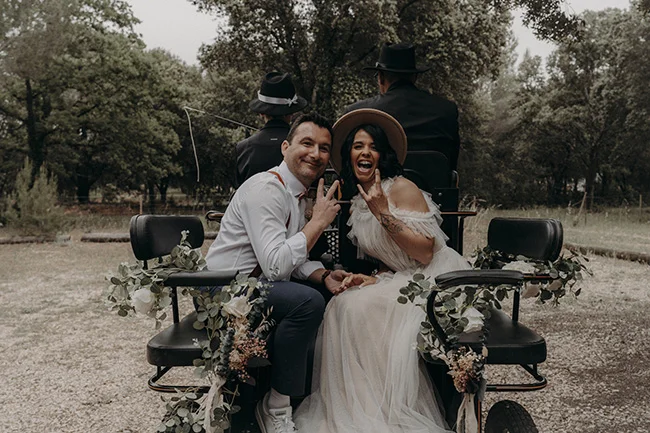 Une mariée et son mari dans un chariot romantique, entourés de verdure luxuriante, dégagent un sentiment de joie et