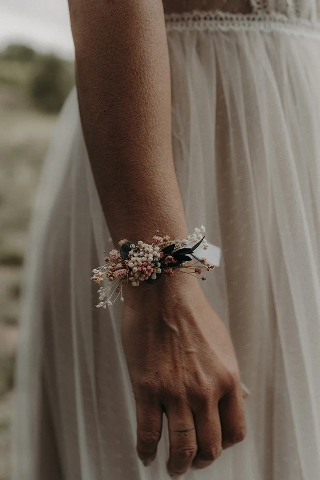 Un poignet délicat orné d'une brindille de fleurs fraîches, allant parfaitement avec l'élégance bohème d'une robe blanche légère.