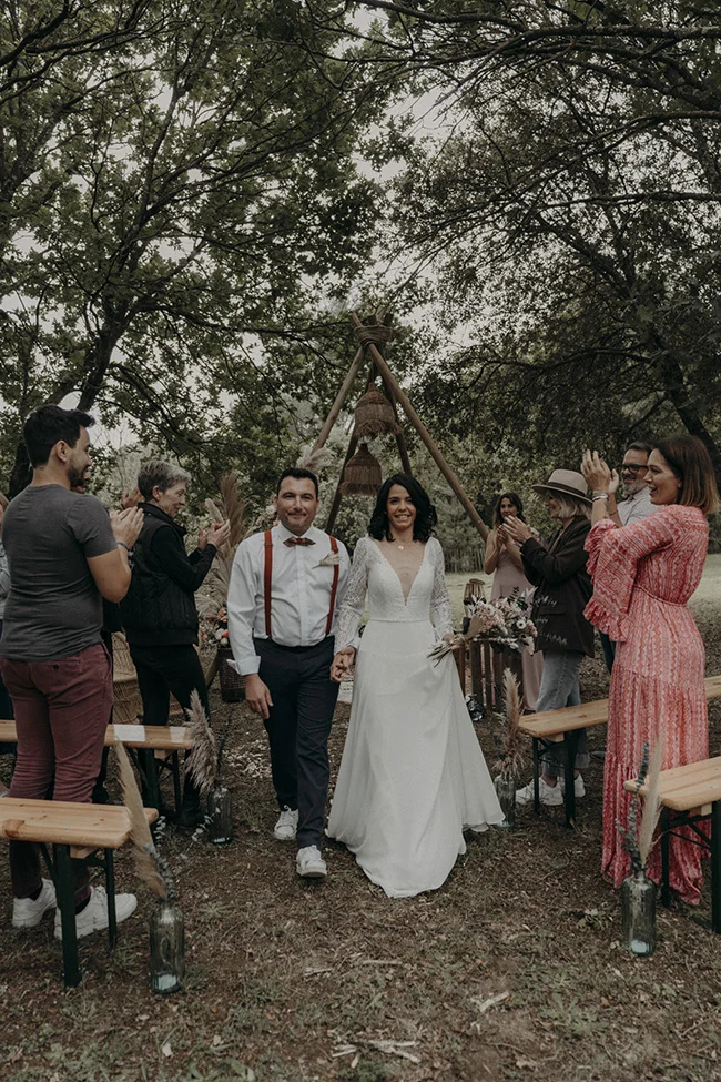 Un mariage bohémien charmant avec un couple heureux et des invités rassemblés autour d'une table en bois, décorée de