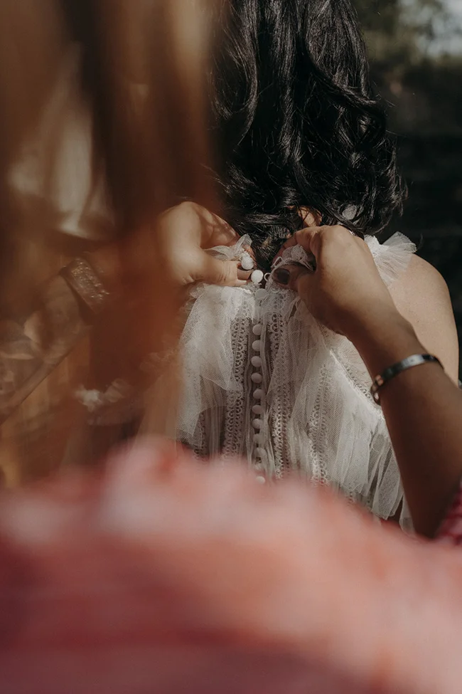 Une jeune femme se prépare dans son robe blanche délicatement brodée, plongée dans la préparation d'un mariage bohémien à Uzès.