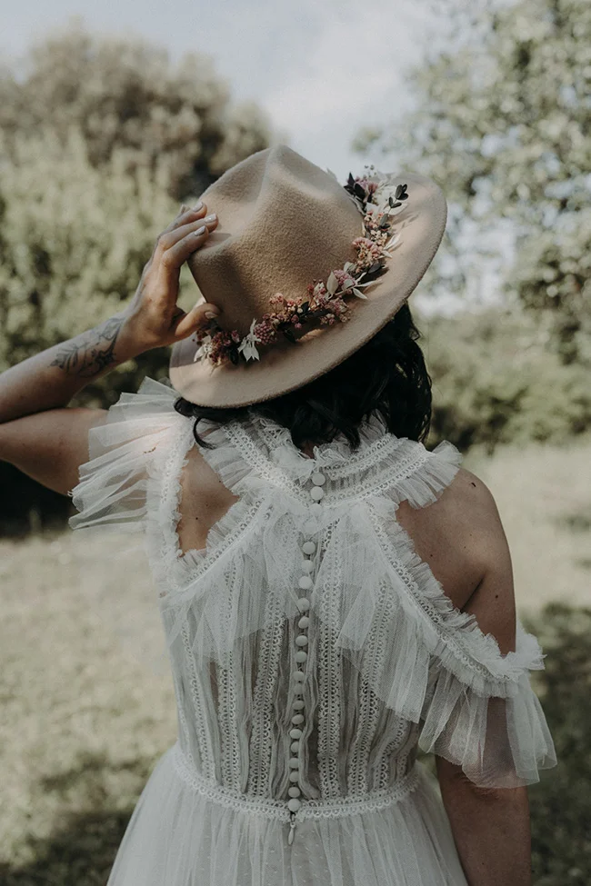 Une mariée en robe blanche bohème et chapeau décoré de fleurs, plonge dans la nature.