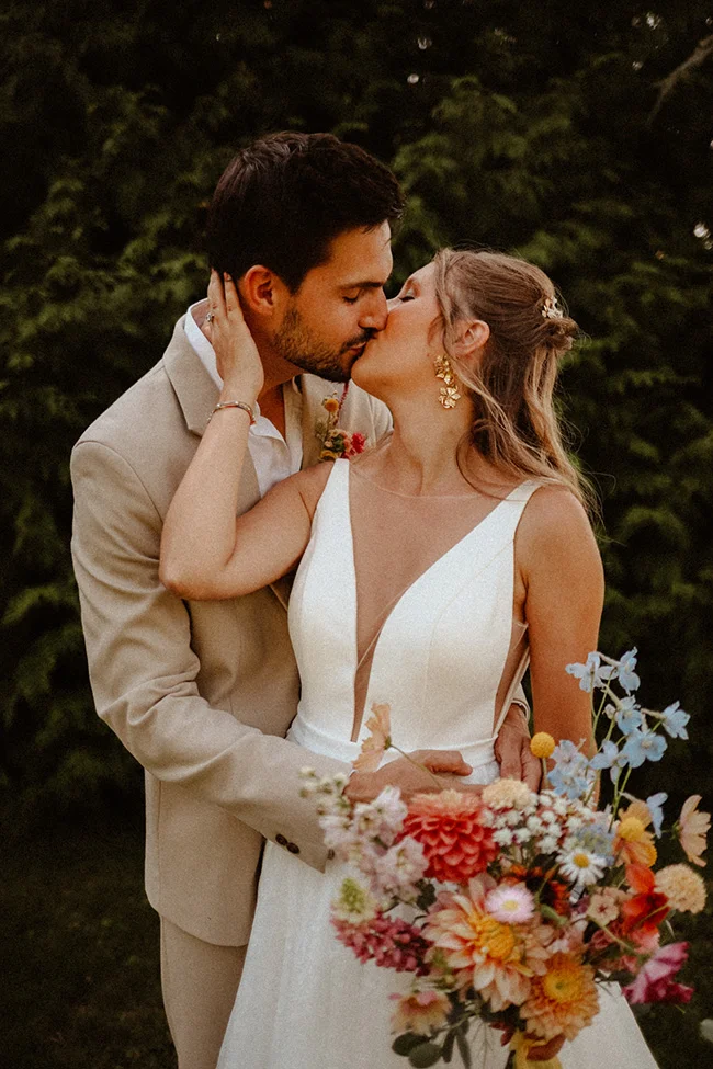 Un mariage intime, léger et coloré, avec un couple heureux et romantique partageant un baiser tendre au milieu des fleurs.