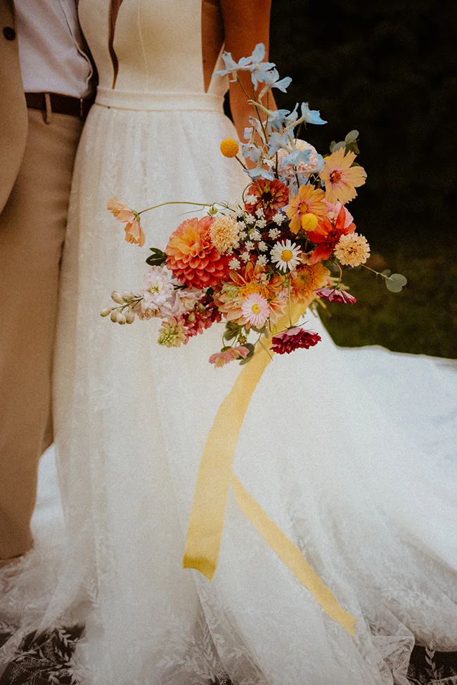 Un bouquet vibrante de fleurs encadrant une robe de mariée blanche, symbolisant un mariage intime, léger et coloré.