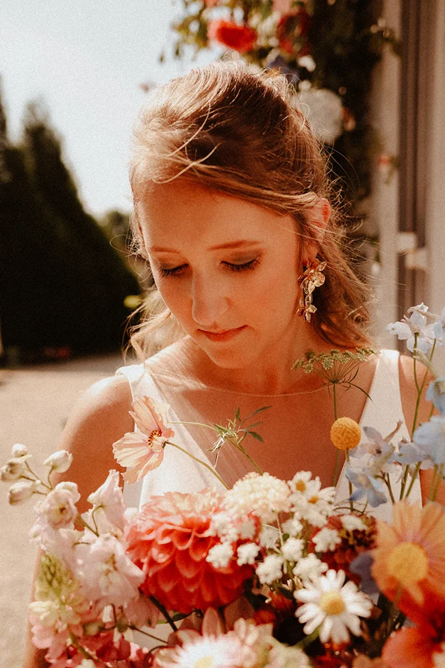 Une jeune femme savoure l'harmonie des fleurs dans ses mains, dans un mariage intime et coloré.