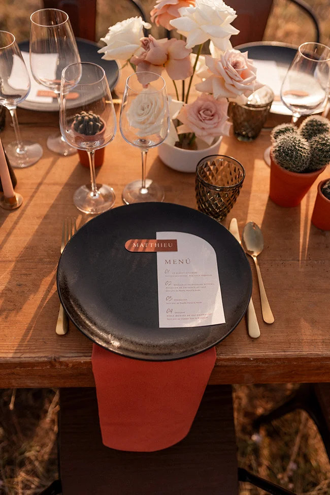 Table de mariage accueillante avec un menu, verres de vin et fleurs blanches, créant un atmosphere chaleureuse et