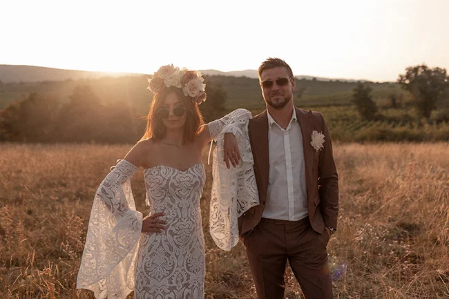 Un couple heureux dans un champ ensoleillé, la mariée dans un robe époustouflante blanc ornée de fleurs blanches et de