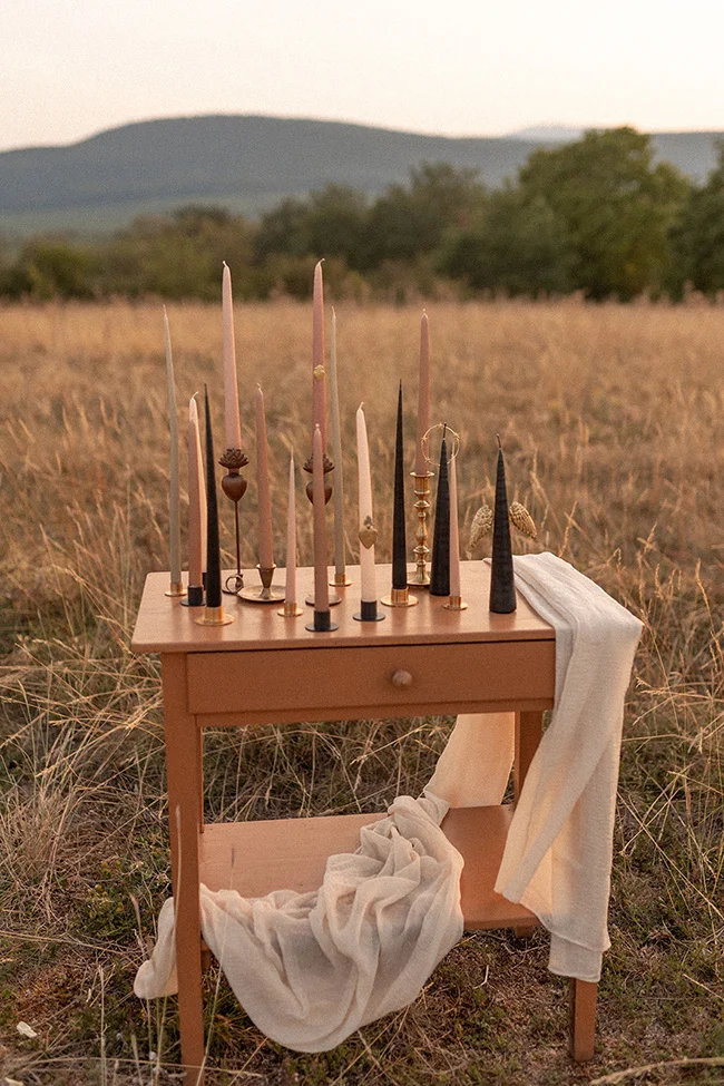 Tableau romantique avec des cierges et des vêtements blancs dans un champ, évoquant un mariage spirituel et coloré.