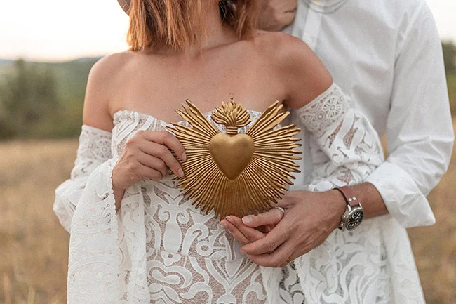 Un couple marié se tient dans une scène romantique, le mari tenant un symbole religieux au cœur doré.
