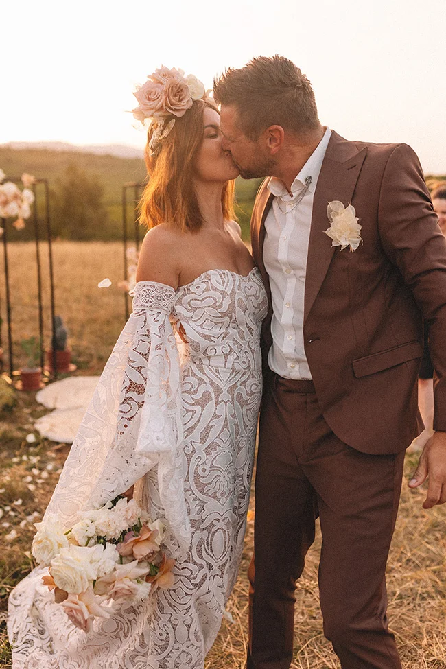 Un couple marié s'embrassant tendrement au coucher de soleil, vêtus de mode romantique pour un mariage spirituel et mexicain.