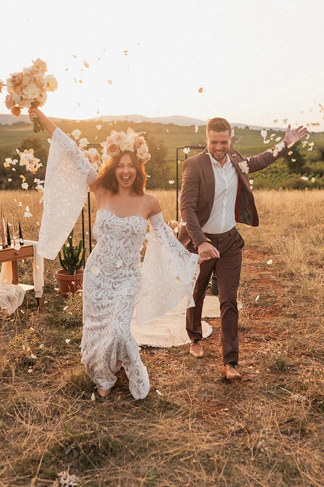 Une mariée exaltée dans un décor champêtre avec son mari, jetant des pétales de fleurs, capturant l'essence d'un