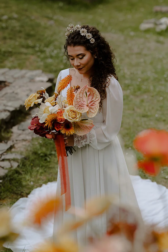 Une jeune femme dans un robe blanche tendue tenant un bouquet magnifique de fleurs dans un décor rustique.
