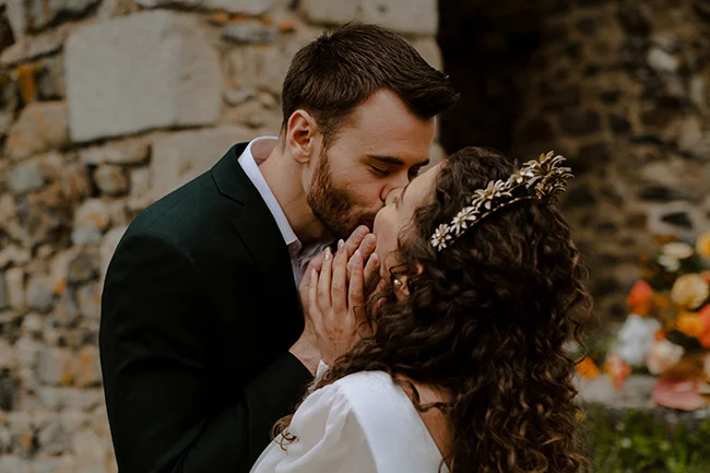 Un couple romantique partage un baiser tendre contre un décor d'ancien mur en pierre, idéal pour un elopement au milieu