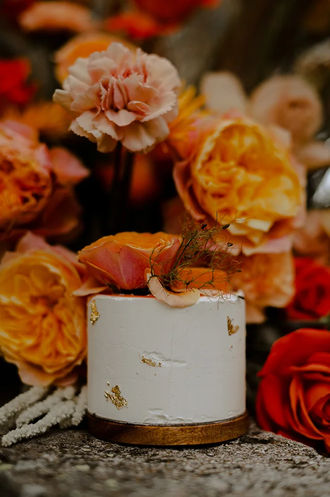 Un petit bol blanc orné de fleurs fraîches et de feuilles d'herbe, entouré de roses et de carnations pour un elopement