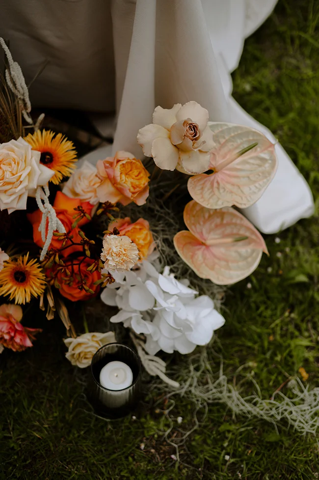 Un bouquet romantique de fleurs blanches et orange avec des papillons fantaisistes et une petite lampe à cire, tout sur