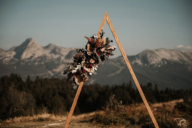 Un témoignage romantique dans les montagnes, avec un bouquet de plumes colorées et un triangle en bois comme décor.