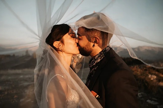Un couple romantique se baigne dans le coucher de soleil, leurs vêtements de mariage éclatant contre les couleurs