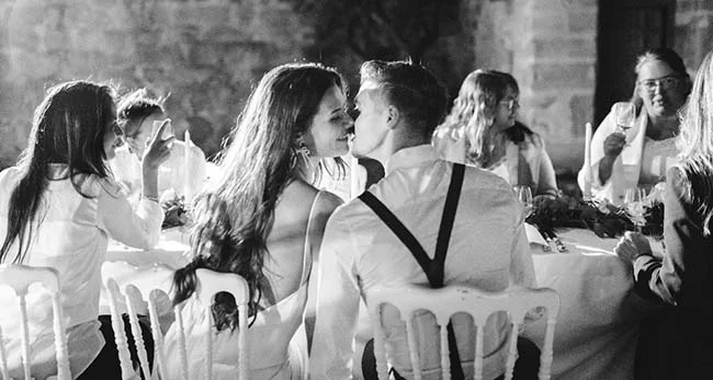 Un couple charmant se regarde l'un l'autre dans des assises blanches, entouré d'invités rassurés dans un décor sombre