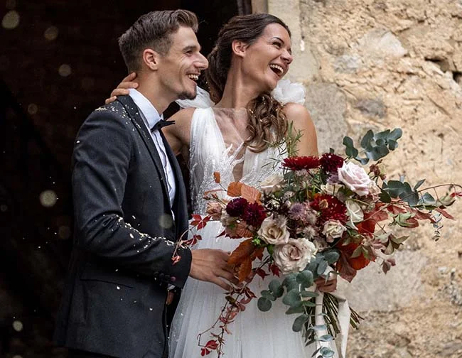 Une jeune mariée dans une robe blanche légère, tenant un bouquet de fleurs raffinées, se détache contre un mari en