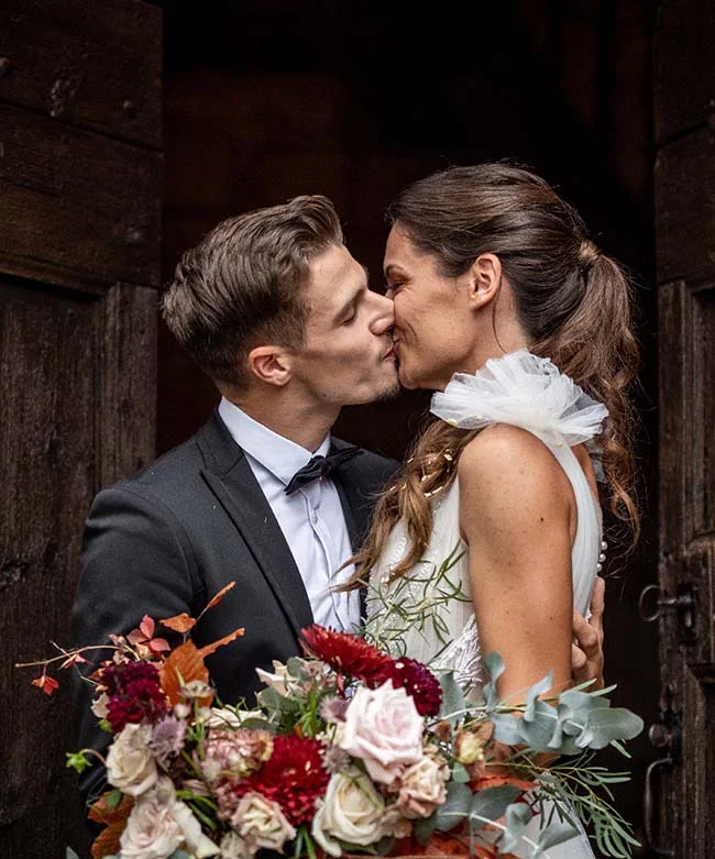 Un couple heureux partage un baiser tendre, entouré d'une bouquet de fleurs élégantes et colorées, dans un décor